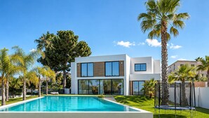 Uma casa moderna de dois andares com piscina, rodeada por palmeiras e um gramado bem cuidado.