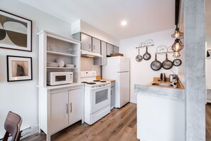 A modern kitchen with white cabinetry, a built-in oven, microwave, and a refrigerator. There are hanging pots and pans on the wall, and a wooden countertop with a sink.