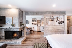 A modern interior with a fireplace, dining area, kitchen, and a bedroom with a large bed.
