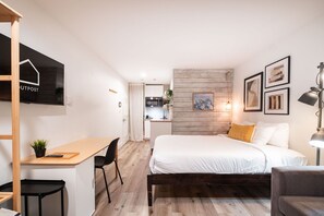 Ein gemütliches Hotelzimmer mit Bett, Schreibtisch, Stuhl, einem kleinen Tisch und einer Couch. Im Hintergrund befindet sich eine Küchenzeile.