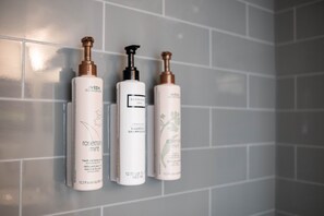 Drie flessen shampoo op een betegelde muur.
