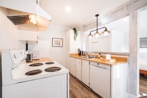 A modern kitchen with white cabinetry, a stove, a dishwasher, and a wooden countertop. - Creekside | Walk to Gondola | Quiet Studio (Whistler)