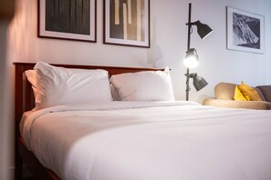 A hotel room with a bed, a bedside lamp, a sofa with cushions, and framed artwork on the walls. - Creekside | Walk to Gondola | Quiet Studio (Whistler)