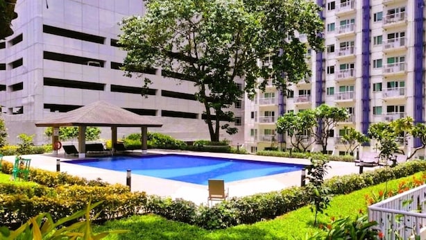A swimming pool surrounded by greenery, a covered seating area, and a multi-story building with balconies. - Grass Residence SM NORTH MRT NLEX PH ARENA (QUEZON CITY)