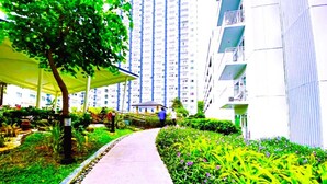 A pathway leading to a residential building with balconies, surrounded by greenery and a covered area. - Grass Residence SM NORTH MRT NLEX PH ARENA (QUEZON CITY)