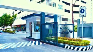 A gated entrance with a blue fence, a pedestrian crossing, and a building with multiple windows in the background.