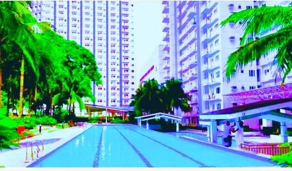 A high-rise residential building with balconies, a swimming pool, and palm trees.