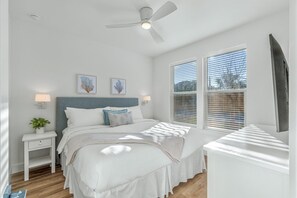 Ein Schlafzimmer mit einem Bett, Nachttischen, einem Deckenventilator und einem Fenster mit Jalousien.