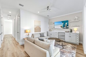 A modern living room with a sofa, coffee table, and a TV mounted on the wall. - Goombays Getaway: Private heated pool, Free golf cart, 1 min to beach, Game room (Miramar Beach)