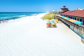 Ein Strand mit einer langen Pier, bunten Sonnenschirmen und Liegestühlen.