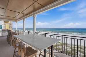 A covered outdoor area with a table and chairs, overlooking a beach with a clear view of the ocean. - Gulf front | Heated Private Pool |Sleeps 18 | Bonfire Incl (Panama City Beach)