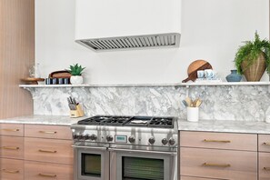 A kitchen with a stainless steel stove, marble countertop, wooden cabinets, and a built-in range hood. - Gulf front | Heated Private Pool |Sleeps 18 | Bonfire Incl (Panama City Beach)