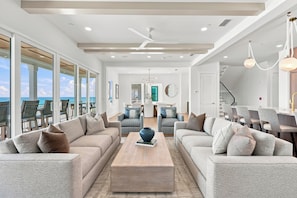 A spacious living room with a large window overlooking the ocean, a dining area with modern furniture, and a kitchen with a view. - Gulf front | Heated Private Pool |Sleeps 18 | Bonfire Incl (Panama City Beach)