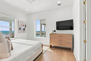 Ein Schlafzimmer mit einem Bett, einer Kommode, einem Fernseher und einem Fenster mit Meerblick.