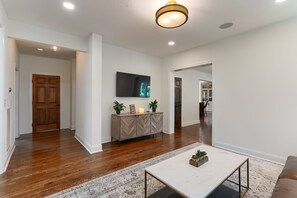 A spacious living area with hardwood floors, a white sofa, a coffee table, and a mounted TV. - 🌸 Magnolia House @ 12 South | Private Pool | Sleeps 10 | Fireplace (Nashville)
