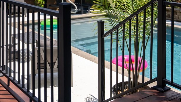 Area piscina con terrazza in legno, ringhiera in metallo e vista su un edificio residenziale sullo sfondo.