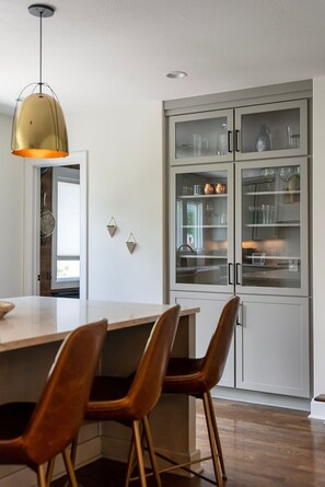 Una cucina moderna con isola in legno, due sgabelli da bar e una lampada a sospensione.