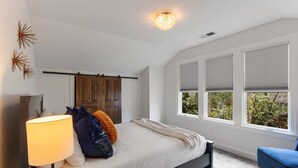 Una camera da letto con un letto, un comodino, una lampada, una finestra con persiane e vista sul verde circostante.