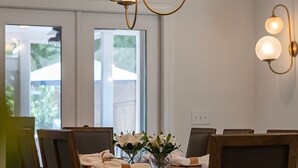 Un'area pranzo con un tavolo di legno apparecchiato per sei persone, circondato da sedie. Sopra il tavolo, un lampadario con diverse lampade.