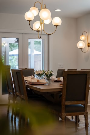 Ein Essbereich mit einem Holztisch, gedeckt für sechs Personen, umgeben von Stühlen. Über dem Tisch hängt eine Chandelüster mit mehreren Leuchten.