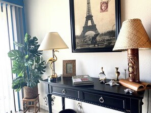 A desk with a lamp, a framed picture of the Eiffel Tower, a potted plant, and decorative items. - 2-bedroom condo-Fun Colorful-Fabulous Rancho Mirage- AC, pools, hot tubs, tennis (Rancho Mirage)