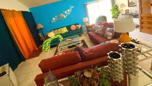 A living room with a blue wall, two sofas, a coffee table, and a lamp. - 2-bedroom condo-Fun Colorful-Fabulous Rancho Mirage- AC, pools, hot tubs, tennis (Rancho Mirage)