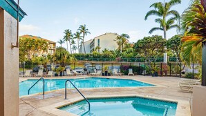 A pool area with two pools, lounge chairs, palm trees, and a building in the background. - Modern Paradise | Kihei 2BR Near Beach (Kihei)