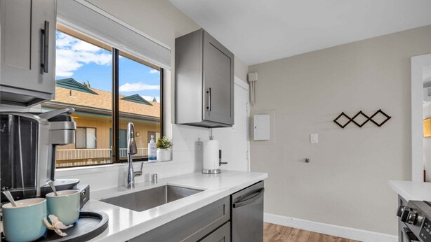 A modern kitchen with a large window, stainless steel appliances, and a view of neighboring buildings. - Modern Paradise | Kihei 2BR Near Beach (Kihei)