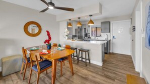 A modern kitchen with a central island, wooden dining table, and chairs. - Modern Paradise | Kihei 2BR Near Beach (Kihei)
