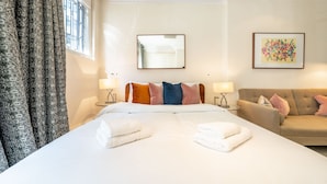 A hotel room with a large bed, a sofa, a mirror, and two wall-mounted lamps. - Royal Studio Apartment in Mayfair (London)