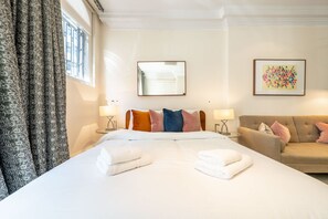 A hotel room with a large bed, a sofa, a mirror, and two wall-mounted lamps. - Royal Studio Apartment in Mayfair (London)