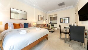 A hotel room with a large bed, a sofa, a dining table with chairs, a TV, and a kitchen area. - Royal Studio Apartment in Mayfair (London)