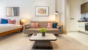 A modern living room with a sofa, a coffee table, and a bed. There is a kitchen area visible to the right. - Royal Studio Apartment in Mayfair (London)
