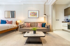 A modern living room with a sofa, a coffee table, and a bed. There is a kitchen area visible to the right. - Royal Studio Apartment in Mayfair (London)