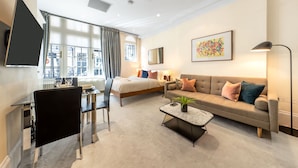 A modern hotel room with a bed, sofa, dining table, and a large window. - Royal Studio Apartment in Mayfair (London)