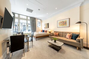 A modern hotel room with a bed, sofa, dining table, and a large window. - Royal Studio Apartment in Mayfair (London)