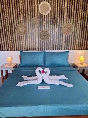 A bed with a teal bedspread, two pillows, and a swan-shaped towel arrangement.