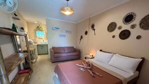 Une chambre à coucher comprenant un lit, une étagère en bois, un ventilateur, une table de chevet et des éléments de décoration murale.