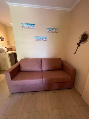 A room with a pink sofa, a small table, and wall decorations including a fan.