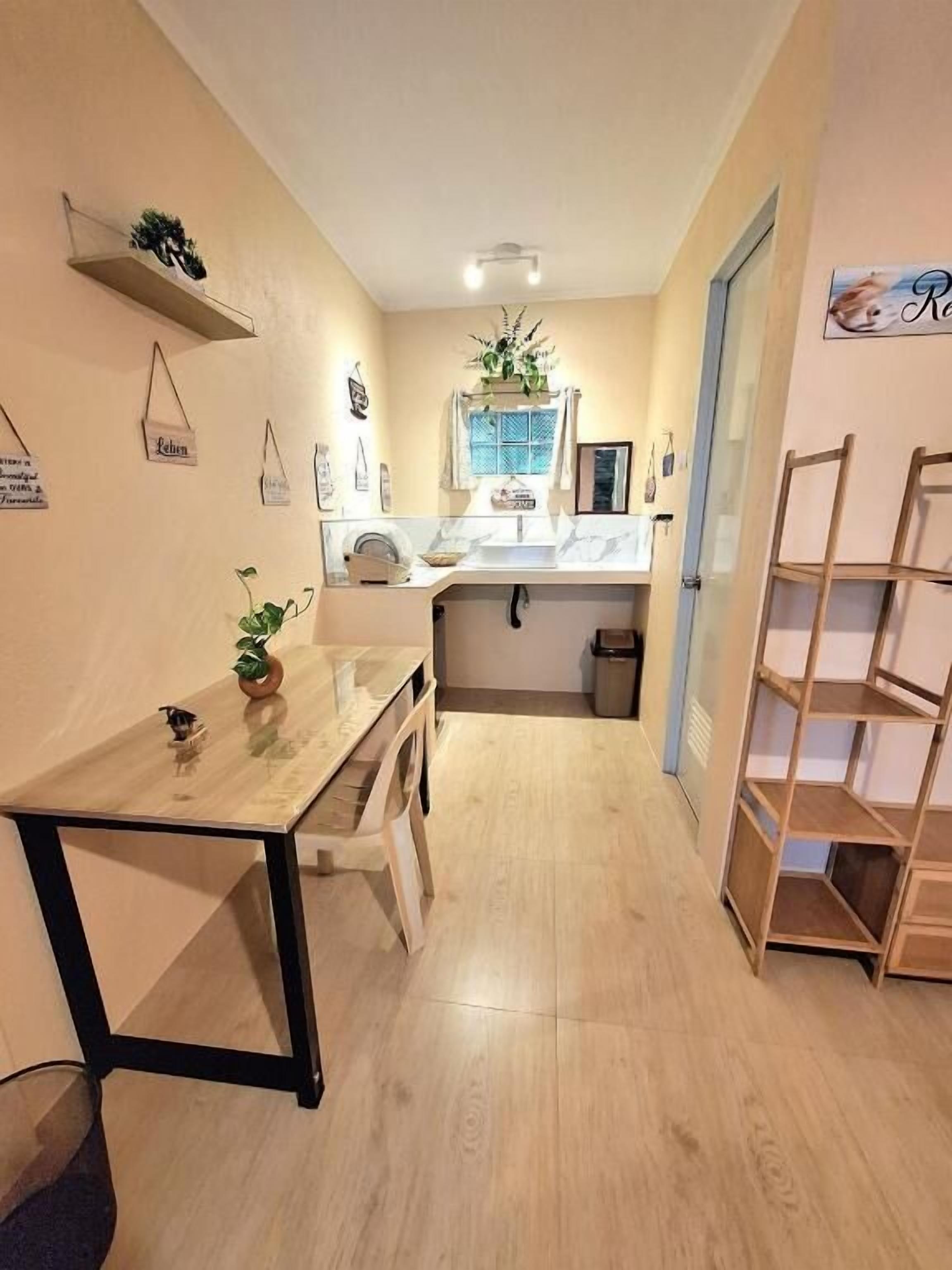 Un pasillo estrecho con suelo de madera, una pequeña mesa con una planta, un armario blanco y una estantería de madera.