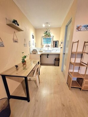 Un pasillo estrecho con suelo de madera, una pequeña mesa con una planta, un armario blanco y una estantería de madera.