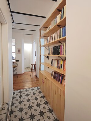 A hallway with a wooden bookshelf filled with books, a tiled floor with a star pattern, and a white door at the end. - 1910 Pera Apartment • 2BR Home • Istiklal & Galata (İstanbul)