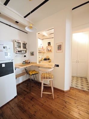 Cocina compacta con encimera de madera, una silla, un refrigerador y una lámpara colgante.