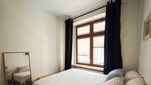 Ein Schlafzimmer mit einem Bett, einem Spiegel, einem Fenster mit Vorhängen und einer Heizung.