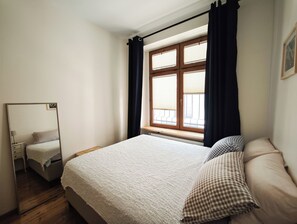 Ein Schlafzimmer mit einem Bett, einem Spiegel, einem Fenster mit Vorhängen und einer Heizung.