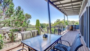 Um deck externo coberto com mesa e cadeiras, rodeado por árvores e uma vista do horizonte.