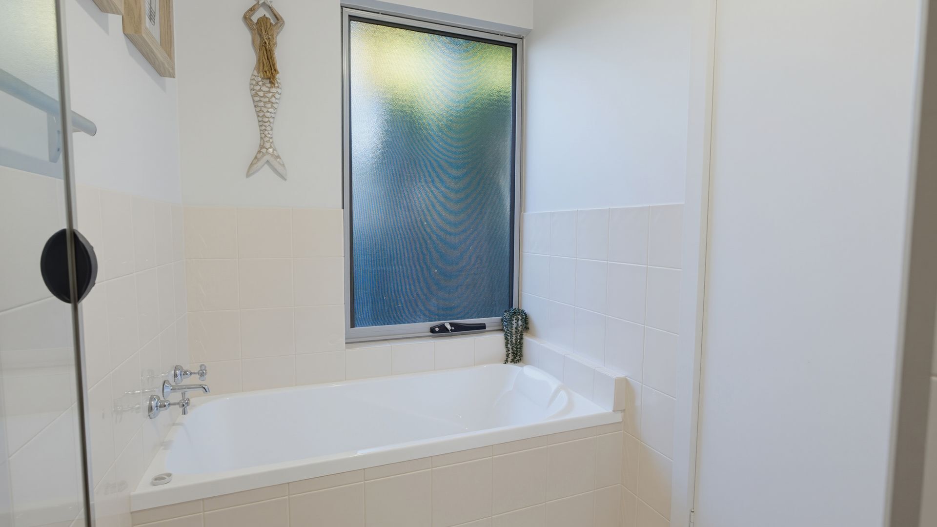 Un bagno con una vasca, una finestra con vista su vetro smerigliato e un porta asciugamani fissato alla parete.