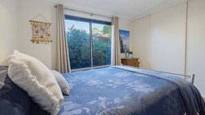 A bedroom with a large bed, a view of trees through a sliding door, and a wall-mounted decoration. - Randalsea - 15 Finniss Vale Drive (Second Valley)