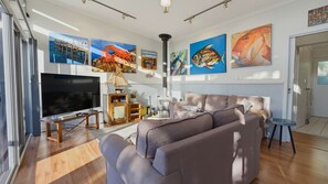 A modern living room with a large flat-screen TV, a sofa, a small table, and a fireplace. - Randalsea - 15 Finniss Vale Drive (Second Valley)