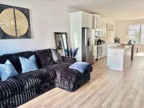 A modern living room with a dark brown sofa, a kitchen with white cabinets, and a large decorative wall piece. - 3-bedroom Townhome in Serene Uptown Charlotte (Charlotte)